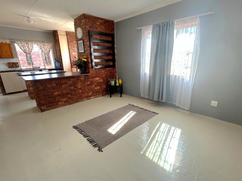 Open-plan living and kitchen area featuring exposed brick accents, built-in cabinetry, and natural light through windows with security bars.