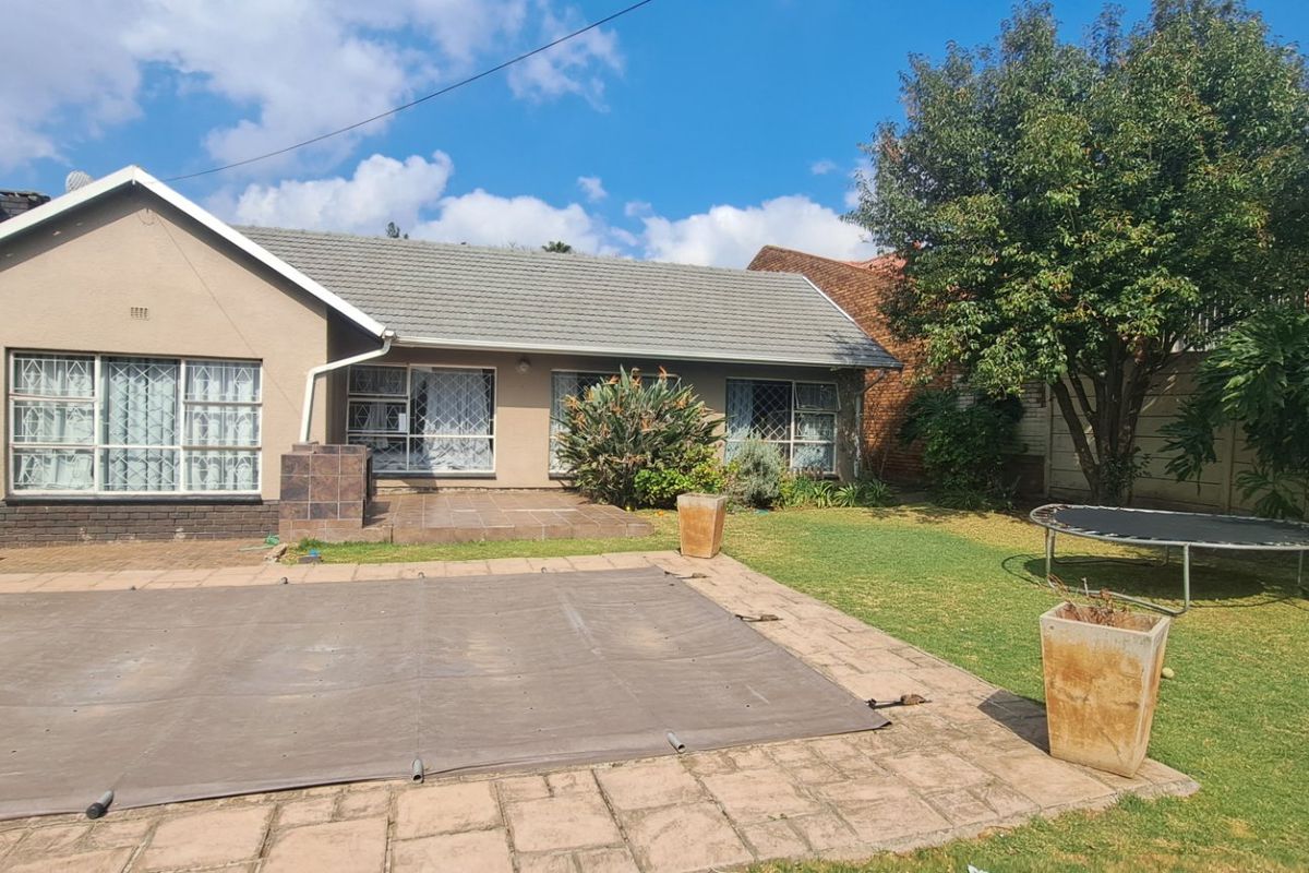 Rear view of the house featuring a swimming pool with cover, paved patio area, and a well-maintained garden with mature trees.