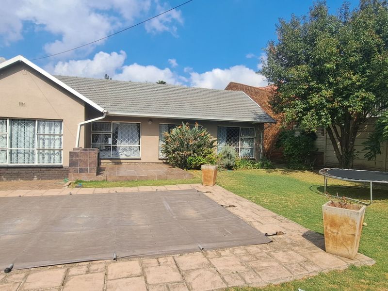 Rear view of the house featuring a swimming pool with cover, paved patio area, and a well-maintained garden with mature trees.