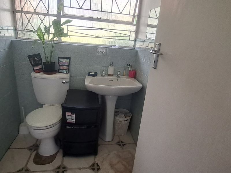 A compact bathroom featuring a pedestal basin, toilet, and dated wall tiling with security bars on the window.