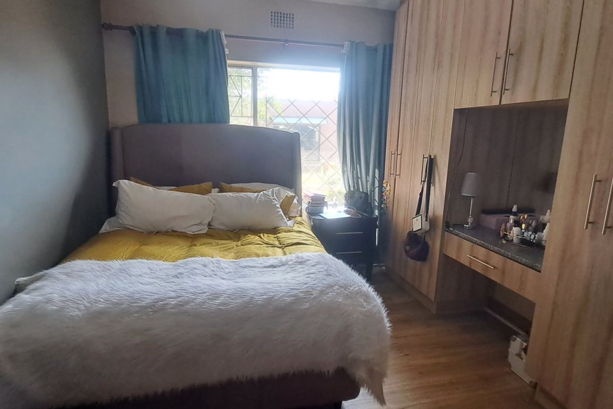 A cozy bedroom featuring light wood-finish built-in cupboards with an integrated vanity desk and durable laminate flooring.