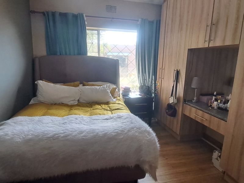 A cozy bedroom featuring light wood-finish built-in cupboards with an integrated vanity desk and durable laminate flooring.