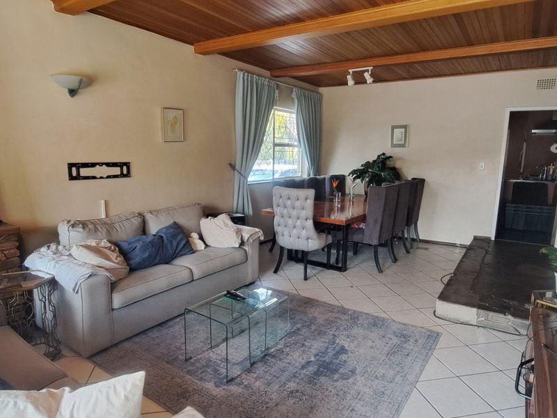 Spacious open-plan living and dining area featuring a timber-clad ceiling with exposed beams, tiled flooring, and a prominent masonry fireplace with a stone hearth.