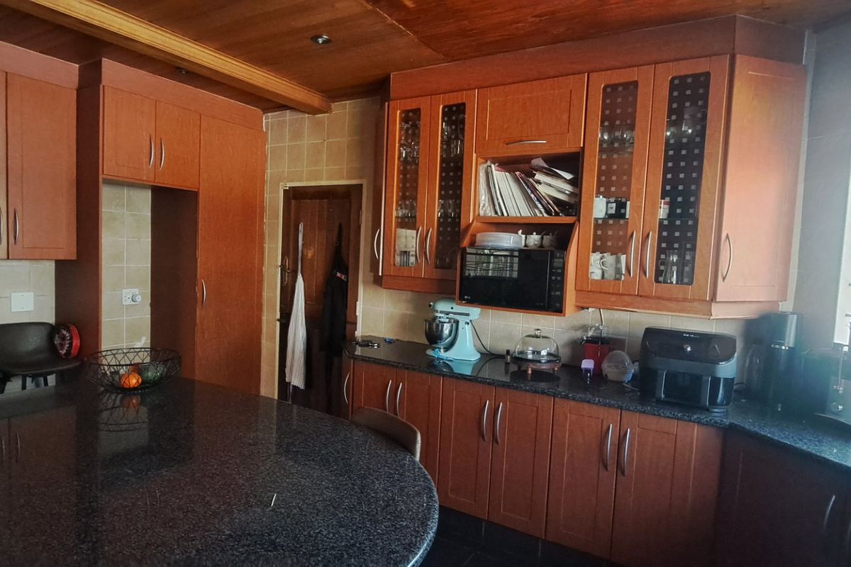 A functional kitchen featuring extensive wooden cabinetry, granite countertops, a tiled backsplash, and a timber ceiling, offering ample storage and workspace.