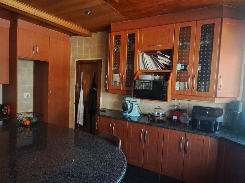 A functional kitchen featuring extensive wooden cabinetry, granite countertops, a tiled backsplash, and a timber ceiling, offering ample storage and workspace.
