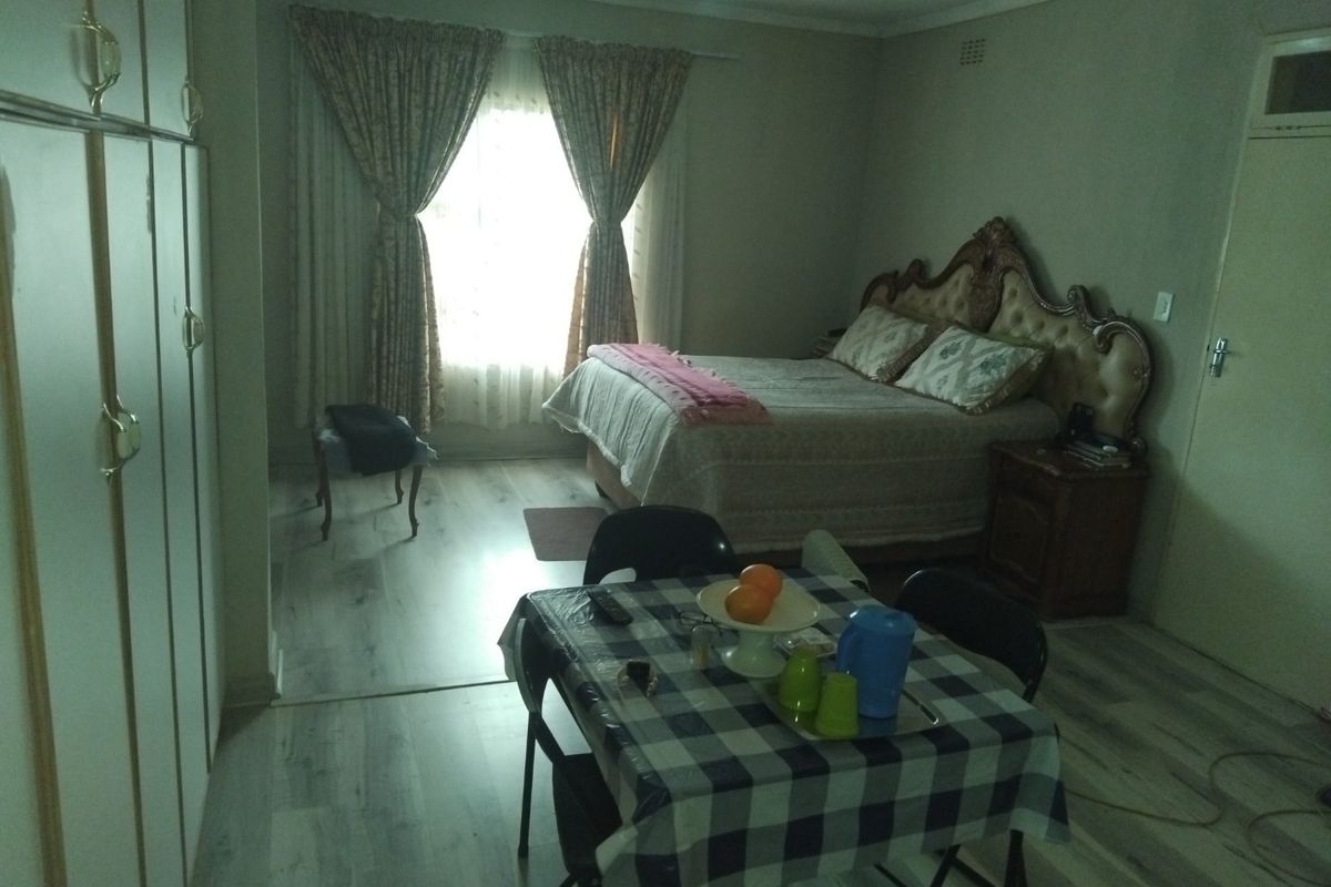 A spacious bedroom featuring light-toned laminate flooring and extensive built-in cupboard storage, offering a functional layout with natural light from the window.