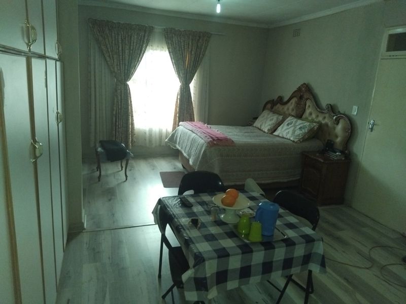 A spacious bedroom featuring light-toned laminate flooring and extensive built-in cupboard storage, offering a functional layout with natural light from the window.