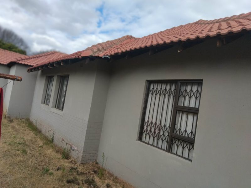 Rear exterior view of the house showing terracotta roof tiles, security gates on windows, and visible maintenance required on the roof eaves and brickwork.
