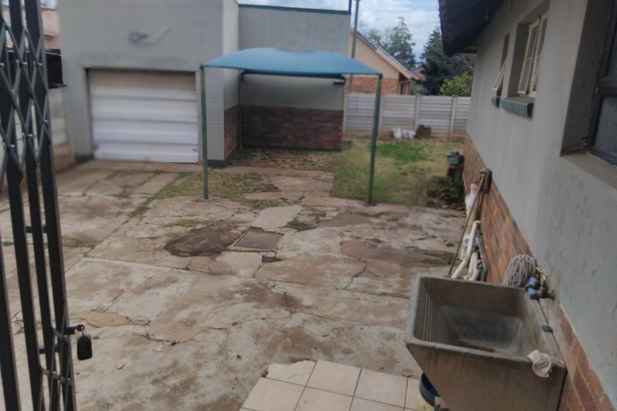 Rear exterior area featuring a garage, concrete paving, a utility sink, and a shade sail structure within a fenced yard.