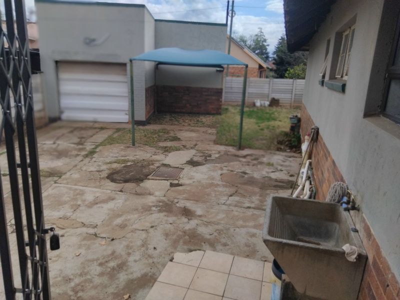 Rear exterior area featuring a garage, concrete paving, a utility sink, and a shade sail structure within a fenced yard.