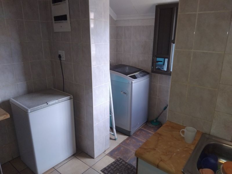 A functional laundry area featuring tiled walls and flooring, a stainless steel sink, and dedicated space for laundry appliances.
