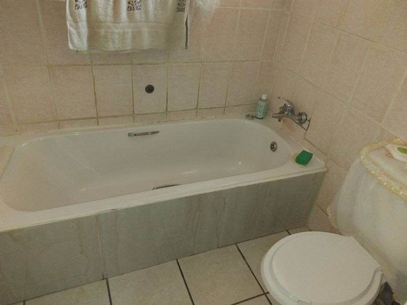 A functional bathroom featuring a built-in bathtub with chrome fixtures and tiled wall and floor finishes.