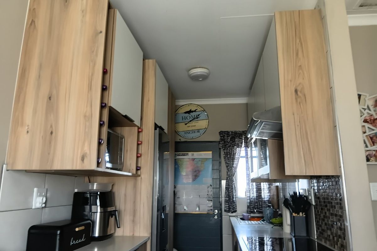 A compact kitchen featuring modern wood-grain cabinetry, a built-in hob, extractor fan, and tiled backsplash, offering a functional and efficient workspace.