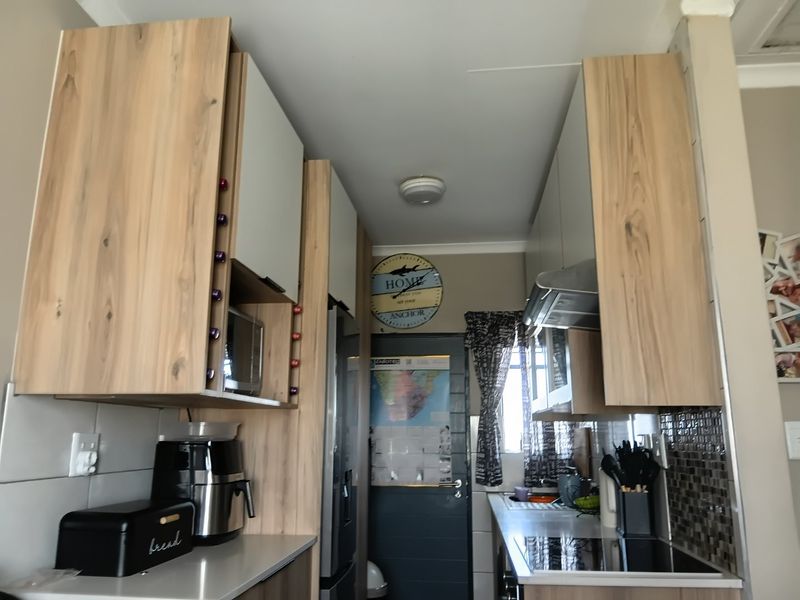 A compact kitchen featuring modern wood-grain cabinetry, a built-in hob, extractor fan, and tiled backsplash, offering a functional and efficient workspace.
