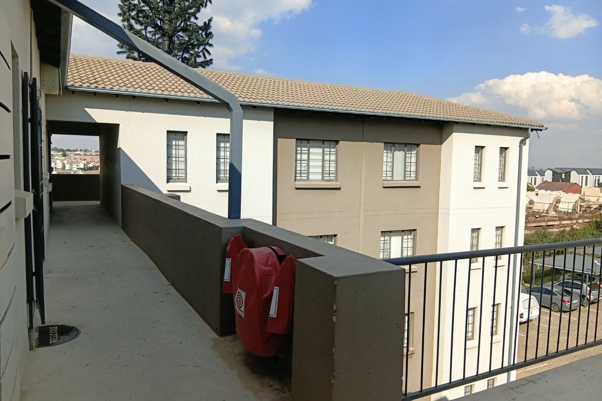 An exterior view of an apartment complex walkway featuring a concrete path, metal safety railings, and a fire hose reel.