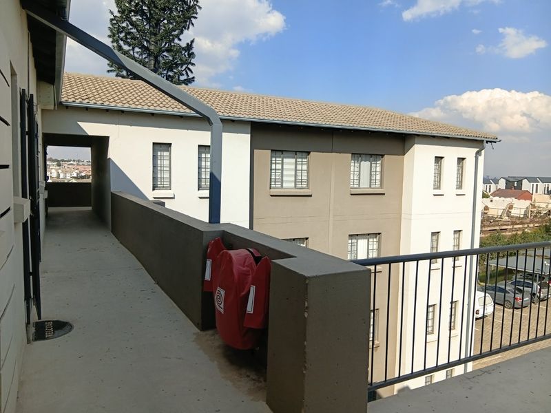 An exterior view of an apartment complex walkway featuring a concrete path, metal safety railings, and a fire hose reel.