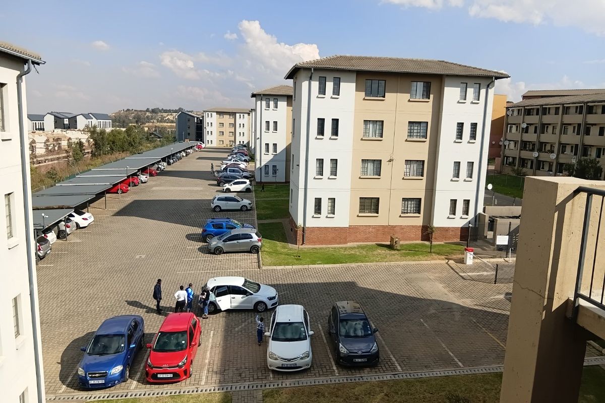An elevated view of an apartment complex featuring paved parking areas, covered parking bays, and multi-story residential buildings with tiled roofs.
