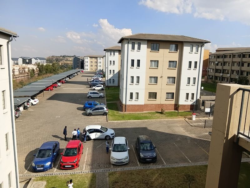 An elevated view of an apartment complex featuring paved parking areas, covered parking bays, and multi-story residential buildings with tiled roofs.