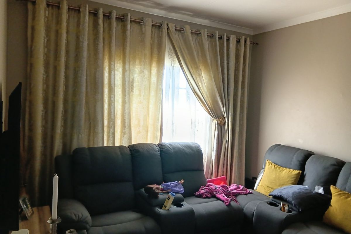 A living room area featuring a window with curtain rod and decorative coving, showing signs of wear on the ceiling and walls.