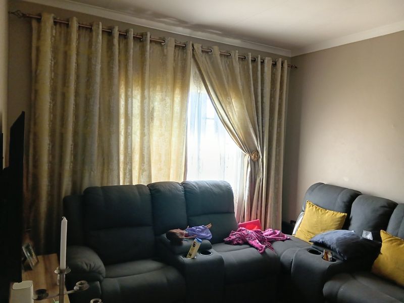A living room area featuring a window with curtain rod and decorative coving, showing signs of wear on the ceiling and walls.