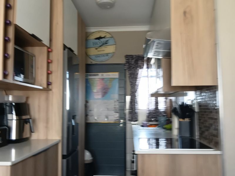 A compact galley-style kitchen featuring modern wood-look cabinetry, tiled backsplash, and integrated appliance housing.