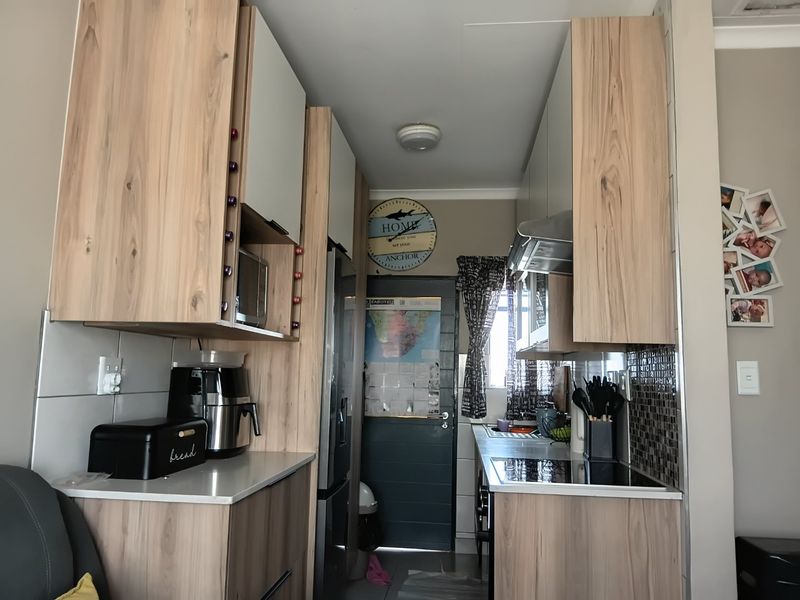 A functional galley-style kitchen featuring modern wood-grain cabinetry, integrated appliances, and a tiled backsplash, providing efficient workspace and storage.