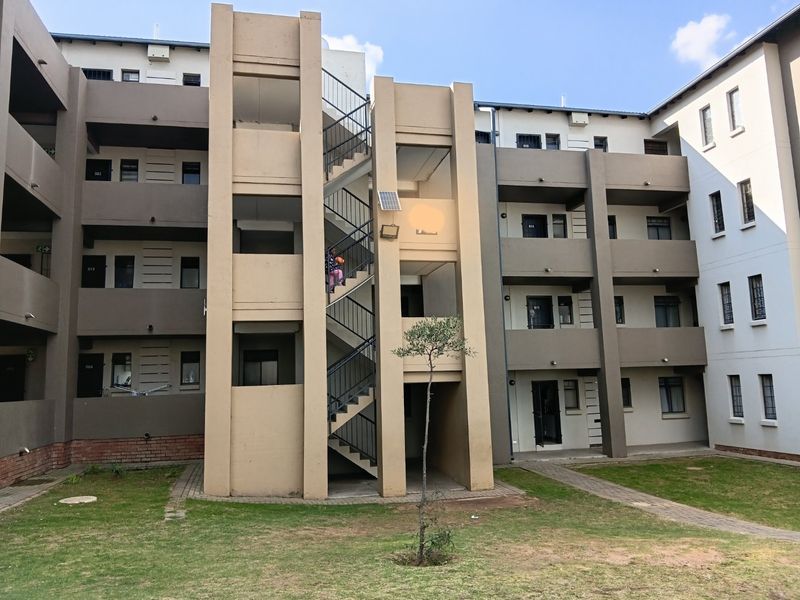 Exterior view of a multi-story apartment complex featuring a central staircase, paved walkways, and landscaped garden area.