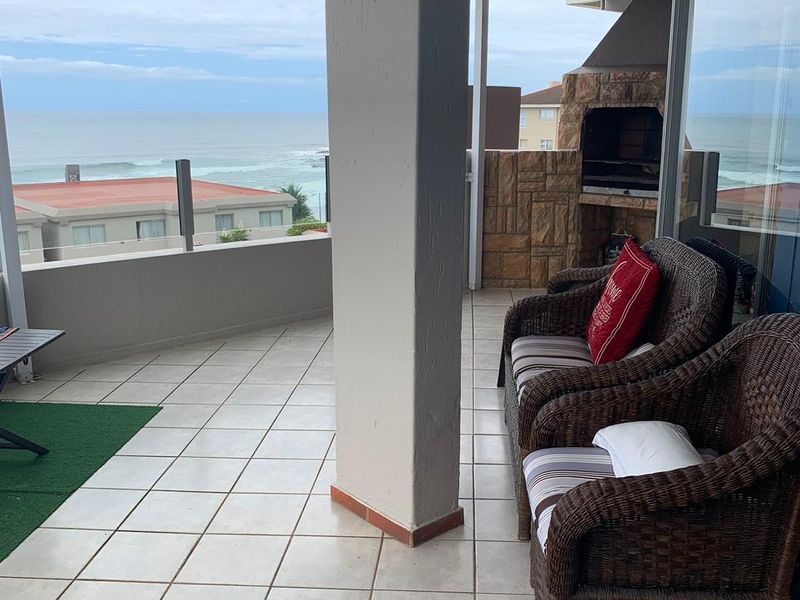 Spacious covered balcony featuring a built-in braai, tiled flooring, and a glass balustrade with scenic ocean views.