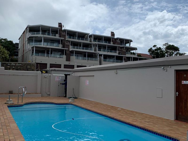 A communal swimming pool area featuring brick paving and boundary walls, set against the backdrop of a multi-story apartment complex.