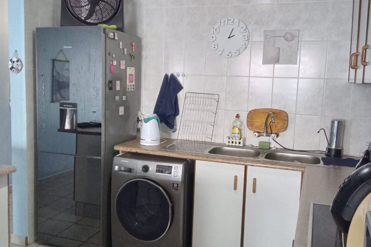 A functional kitchen area featuring a double bowl stainless steel sink, tiled splashback, laminate countertops, and built-in cabinetry with ceramic floor tiles.