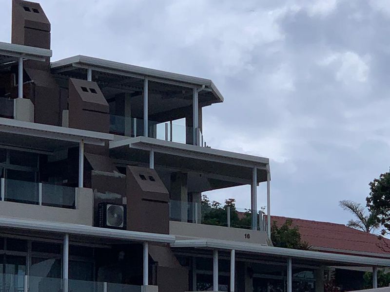 Exterior view of a multi-story apartment building featuring tiered balconies with glass balustrades and external air conditioning units.