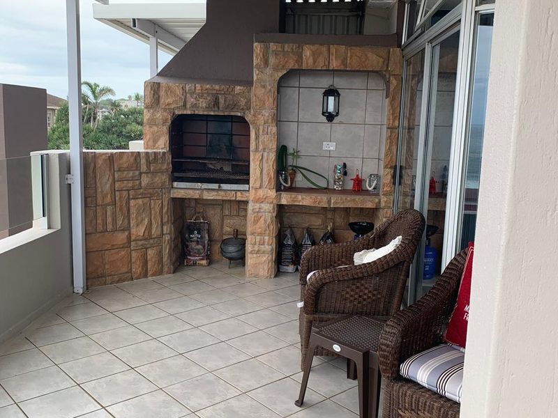 Covered balcony featuring a built-in stone-clad braai area, tiled flooring, and direct access to the apartment interior via large glass sliding doors.