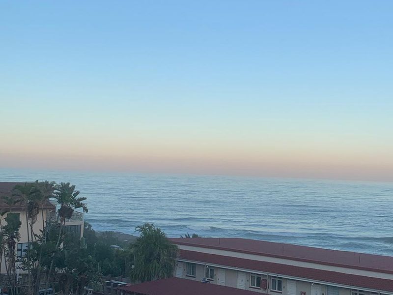Elevated view overlooking the ocean, featuring residential buildings with covered parking structures and tiled roofing.