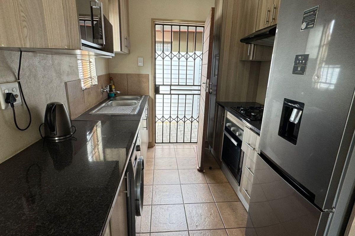 Compact galley-style kitchen featuring granite countertops, built-in cabinetry, integrated oven and hob, and direct access to an exterior security gate.