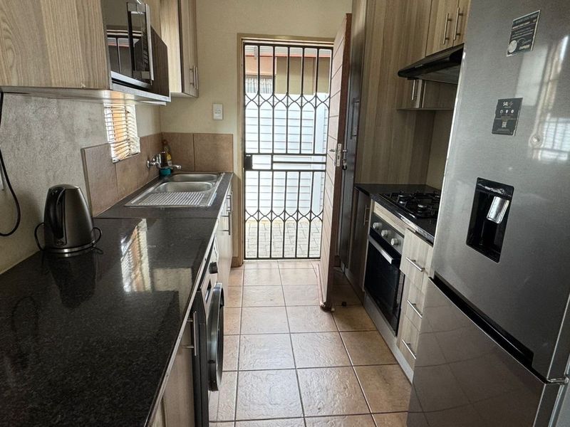 Compact galley-style kitchen featuring granite countertops, built-in cabinetry, integrated oven and hob, and direct access to an exterior security gate.