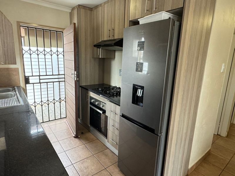A functional kitchen featuring laminate cabinetry, granite countertops, a built-in oven with gas hob, and direct access to an exterior security gate.