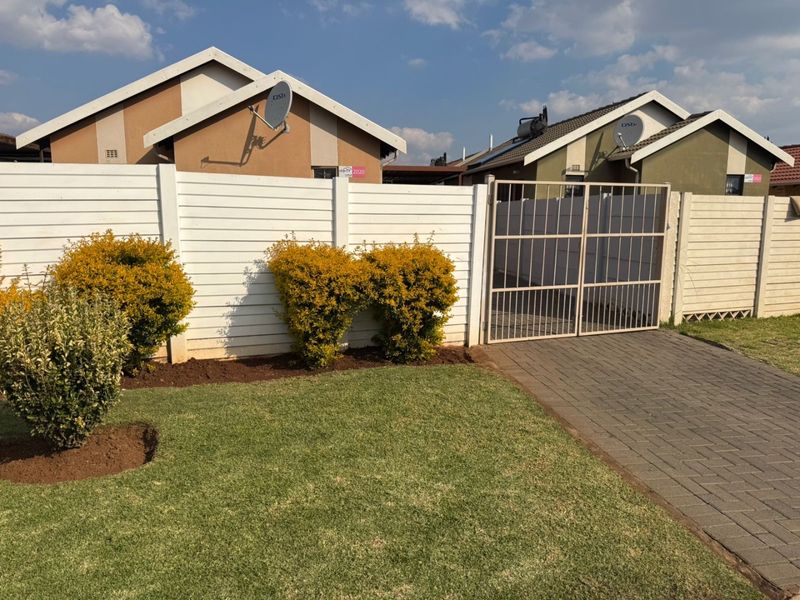 Front view of the property featuring a paved driveway, metal gate, and a well-maintained lawn with a precast boundary wall.