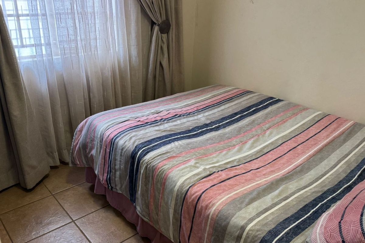 A functional bedroom featuring tiled flooring and window treatments, providing a neutral base for personalization.