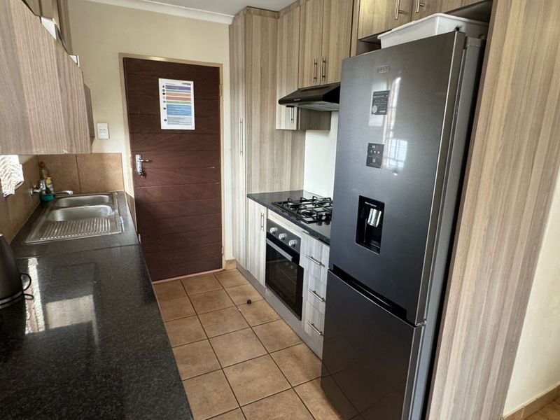 Compact kitchen featuring wood-look cabinetry, granite countertops, gas hob, built-in oven, and tiled flooring, providing a functional and efficient workspace.