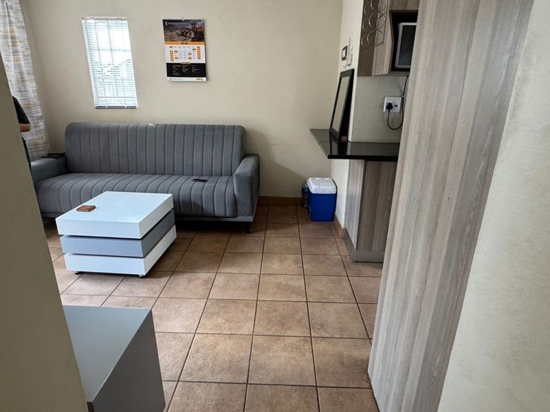 Open plan living area featuring tiled flooring, a built-in breakfast bar, and natural light through venetian blinds.