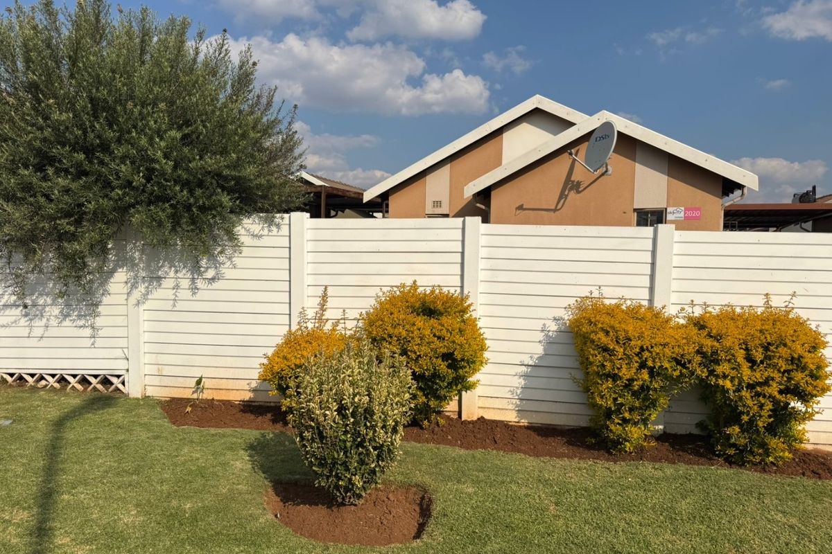 A well-maintained rear garden featuring a white precast concrete boundary wall and established landscaping with a clear view of the house exterior.