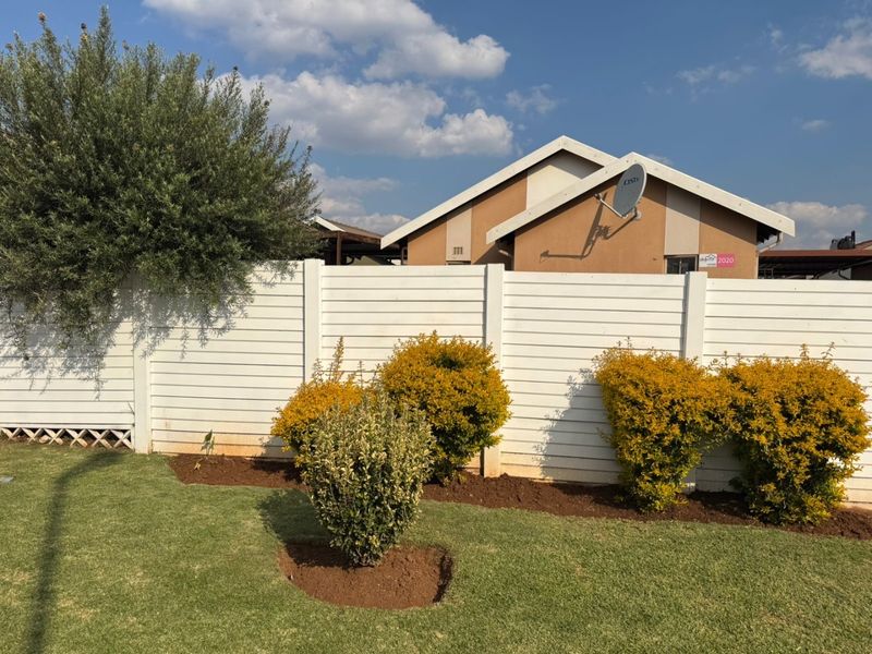 A well-maintained rear garden featuring a white precast concrete boundary wall and established landscaping with a clear view of the house exterior.