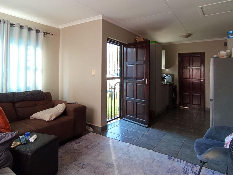 Open plan living area featuring tiled flooring, a security gate entrance, and direct access to the kitchen and rear exterior.