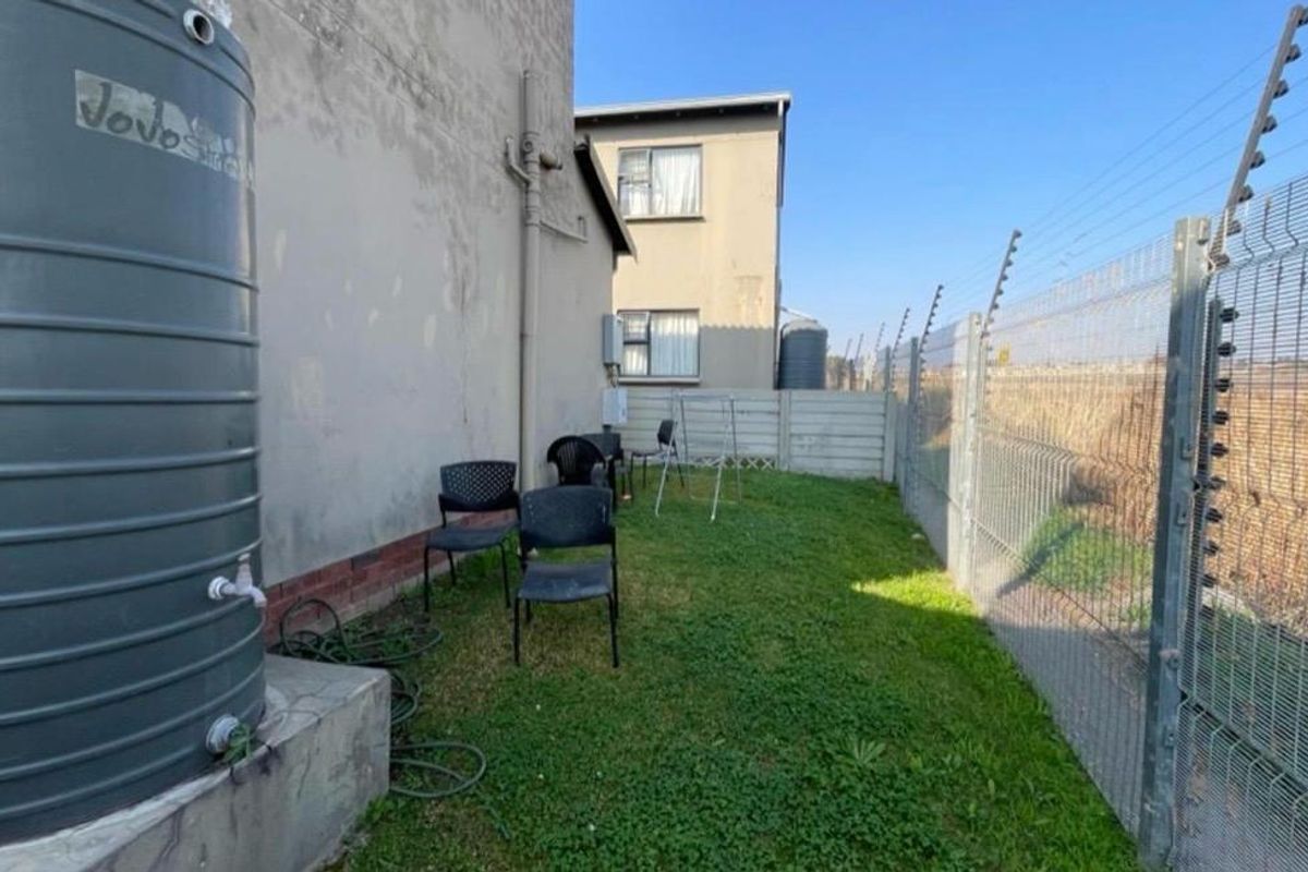 Rear exterior area featuring a water storage tank on a concrete plinth, enclosed by mesh perimeter fencing with electric security wires.