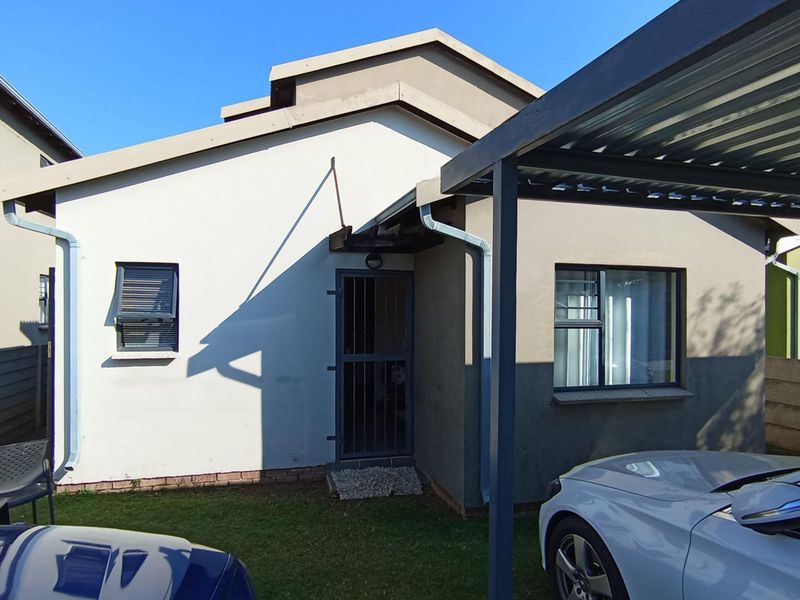 Front elevation of the townhouse featuring a covered carport, security gate entrance, and low-maintenance exterior finishes.
