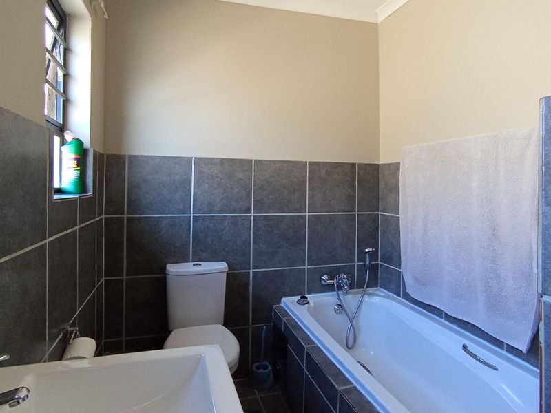 A functional bathroom featuring dark grey wall tiles, a white bathtub with a handheld shower attachment, a standard toilet, and a modern basin.