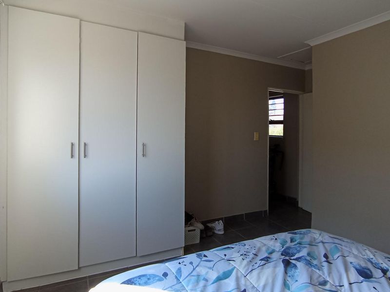 A bedroom featuring built-in cupboards, tiled flooring, and neutral wall tones, providing a functional and clean living space.