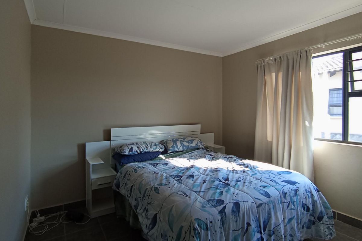 A functional bedroom featuring tiled flooring, neutral wall tones, and a window fitted with security bars.