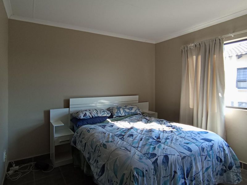 A functional bedroom featuring tiled flooring, neutral wall tones, and a window fitted with security bars.