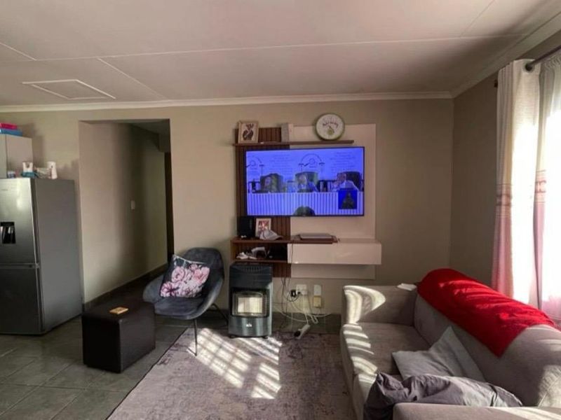 Open-plan living area featuring tiled flooring and an integrated kitchen space with built-in cabinetry and oven, flowing into a comfortable lounge area.